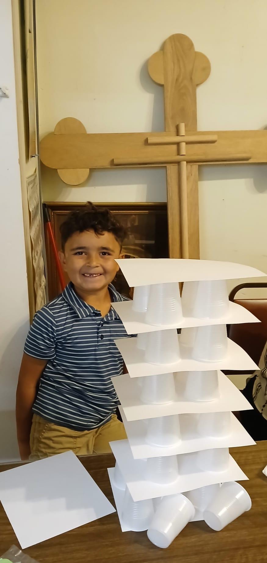 Boy smiling proudly beside his Tower of Babel — Orthodox cross on the wall behind him