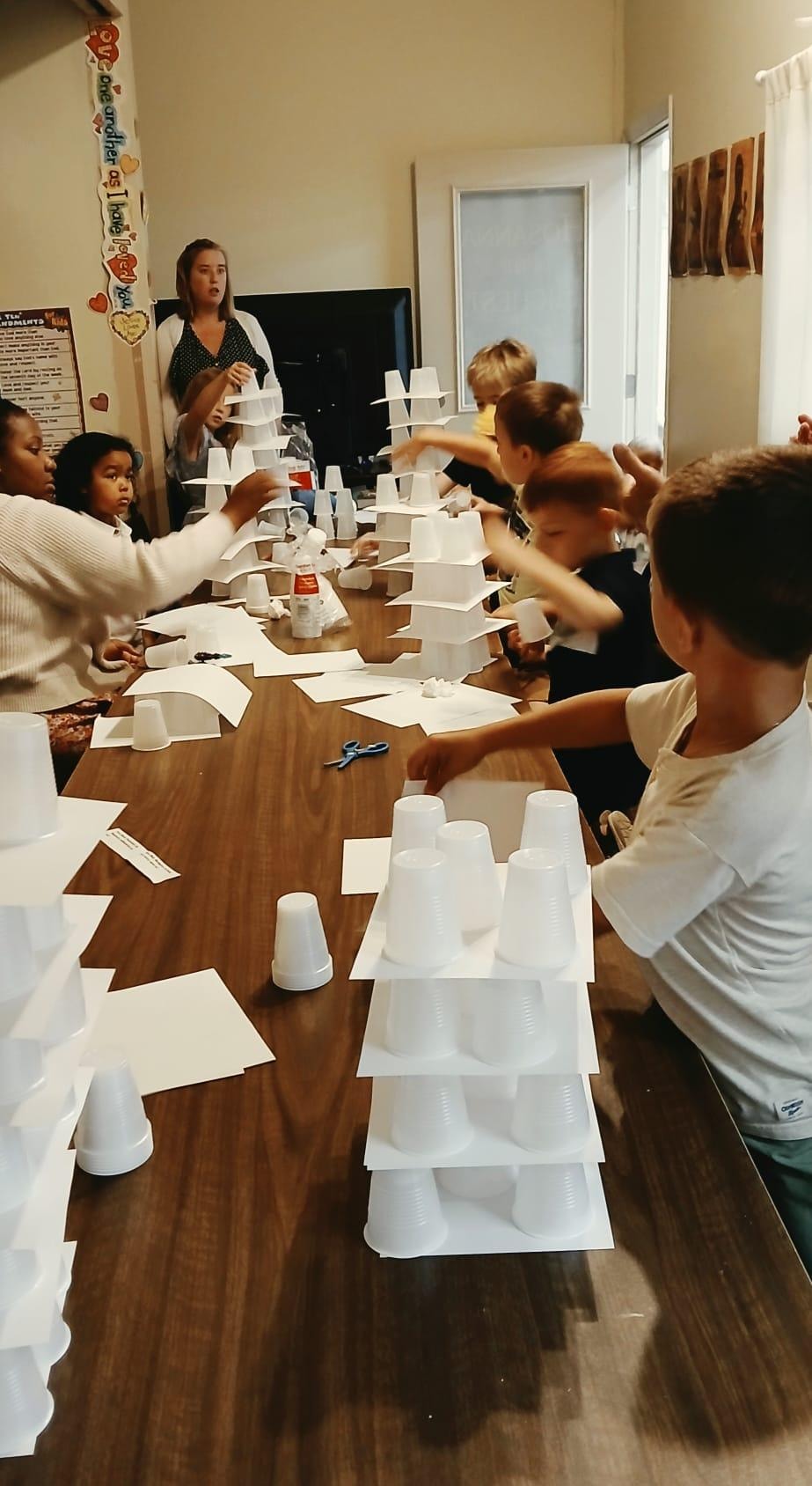 Children and parents building Tower of Babel structures at the Sunday School table — cups and paper towers everywhere